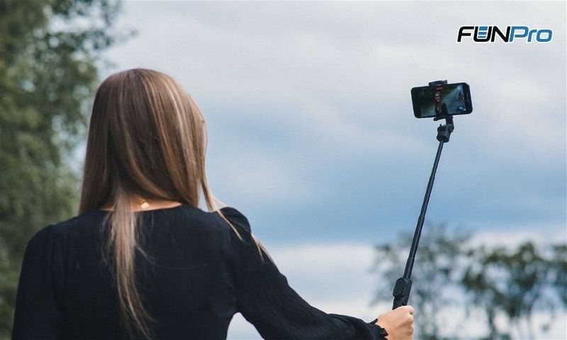 mulher tirando foto com celular em um bastao de selfie