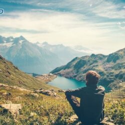 pessoa sentada olhando uma paisagem com montanhas, lagos e grama