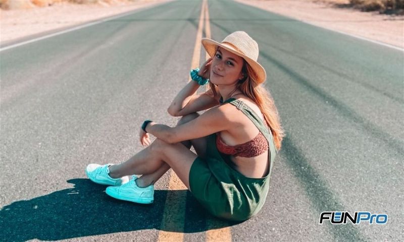 Mulher com chapéu sentada no meio de uma rodovia com perspectiva de continuidade da estrada