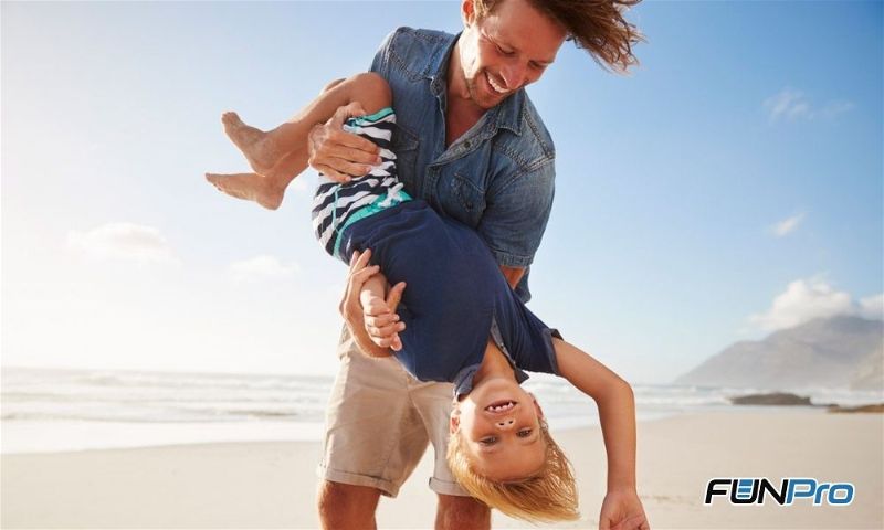 Homem em movimento brincando de girar uma criança com praia ao fundo