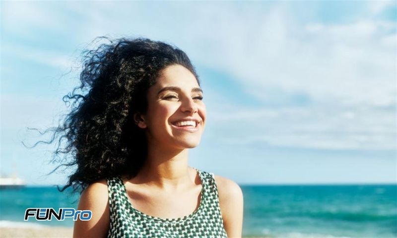 garota sorrindo com a praia ao fundo e o sol batendo na cara