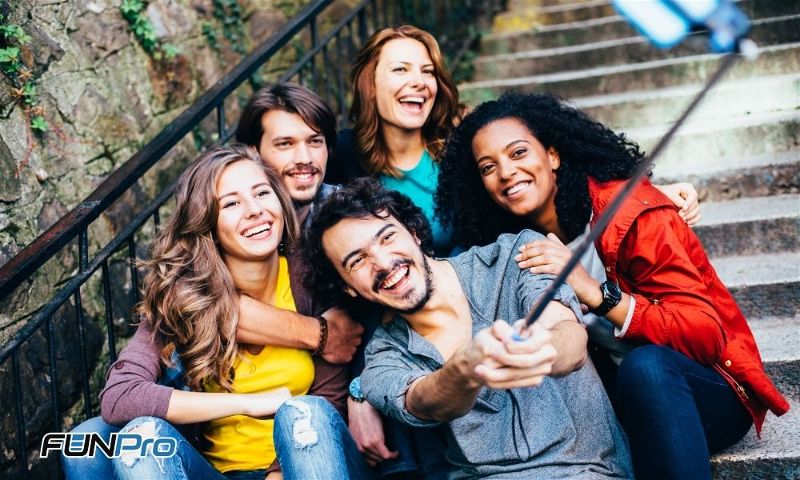 Cinco pessoas tirando uma foto em grupo com o auxilio de um bastão de selfie